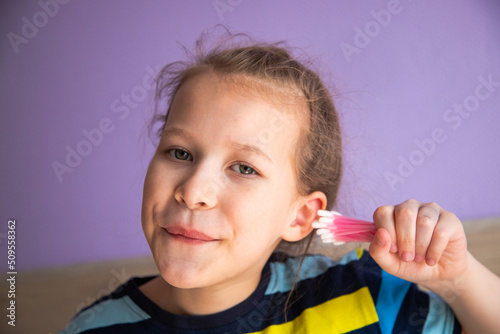 a child girl in a striped turtleneck puts a lot of cotton sticks in her ear, not much dirt will fit