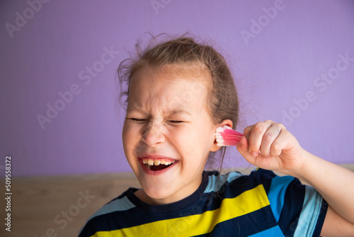 a child girl in a striped turtleneck puts a lot of cotton sticks in her ear, not much dirt will fit