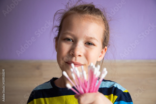 girl child in a striped turtleneck shows cotton swabs for ears