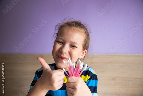 girl child in a striped turtleneck shows cotton swabs for ears