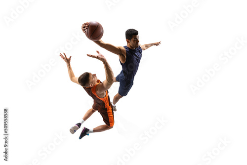 Full-length portrait of two young men, professional basketball players in motion, in a jump throwing a ball isolated over white studio background