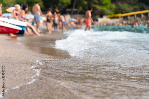 Sandy beach with spalshing waves and people swimming and enjoying summer vibes