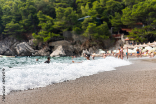 Fototapeta Naklejka Na Ścianę i Meble -  Sandy beach with spalshing waves and people swimming and enjoying summer vibes