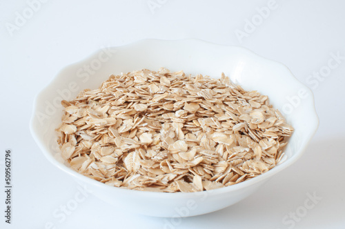 Oat flakes, angled profile view of natural healthy morning breakfast in white bowl. Vegan food isolated on white background.