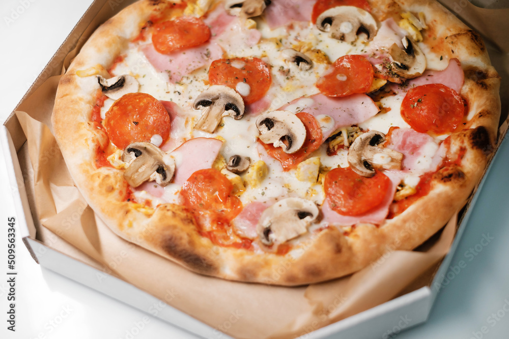 Italian pizza with salami and mushrooms and ham in a cardboard box. The process of making pizza. Street food cooking concept. Italian pizza with salami and mushrooms and ham in a cardboard box. The process of making pizza. Street food cooking concept.