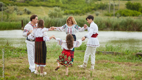 Happy family with kids in traditional romanian dress in a countryside, park. Father, mother, son and daughters dancing outside.