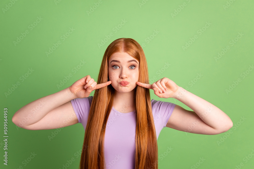 Photo of young pretty girl have fun fingers touch pouted cheeks hold breath fool isolated over green color background