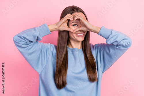 Portrait of attractive girly cheerful girl showing looking through heart symbol isolated over pink pastel color background photo
