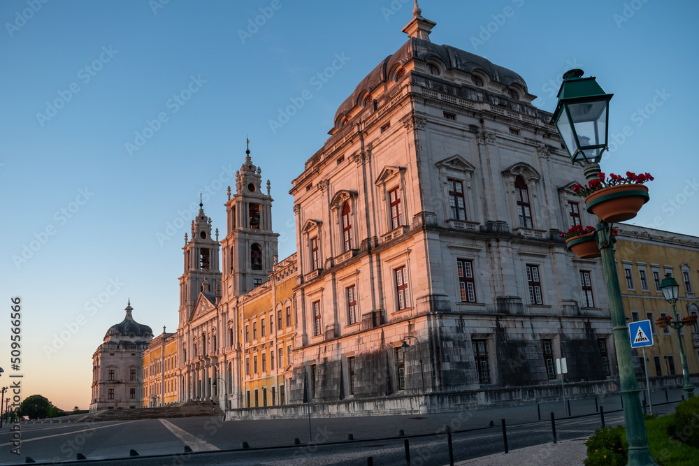 Street with lamps and vases with selective focus by turret with bulbous roof in perspective and facade of the national convent palace of Mafra at golden hour, PORTUGAL