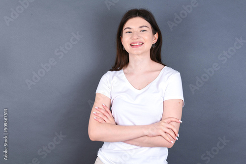 young beautiful Caucasian woman wearing white T-shirt over grey wall being happy smiling and crossed arms looking confident at the camera. Positive and confident person.