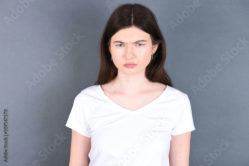 young beautiful Caucasian woman wearing white T-shirt over studio grey wall frowning his eyebrows being displeased with something.