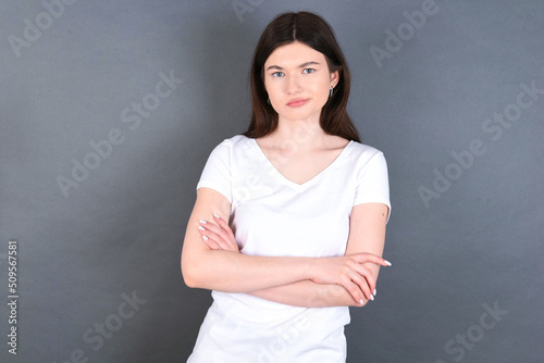 young beautiful Caucasian woman wearing white T-shirt over studio grey wall bitting his mouth and looking worried and scared crossing arms, worry and doubt.