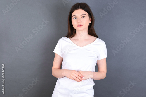 Business Concept - Portrait of young beautiful Caucasian woman wearing white T-shirt over studio grey wall holding hands with confident face.