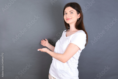 young beautiful Caucasian woman wearing white T-shirt over studio grey wall Inviting to enter smiling natural with open hands. Welcome sign.