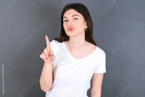 No sign gesture. Closeup portrait unhappy young beautiful Caucasian woman wearing white T-shirt over studio grey wall raising fore finger up saying no. Negative emotions facial expressions, feelings.