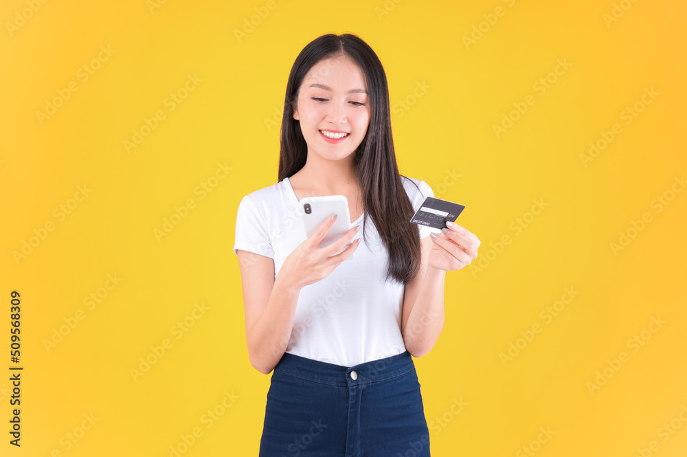 pretty asian woman smile showing, presenting credit card for payment or paying online in holding mobile phone payment credit card for confident money and financial concepts yellow background. pretty asian woman smile showing, presenting credit card for payment or paying online in holding mobile phone payment credit card for confident money and financial concepts yellow background.
