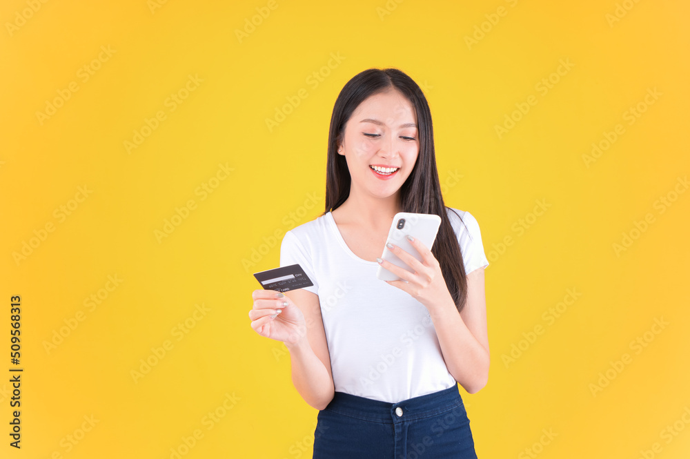 pretty asian woman smile showing, presenting credit card for payment or paying online in holding mobile phone payment credit card for confident money and financial concepts yellow background. pretty asian woman smile showing, presenting credit card for payment or paying online in holding mobile phone payment credit card for confident money and financial concepts yellow background.