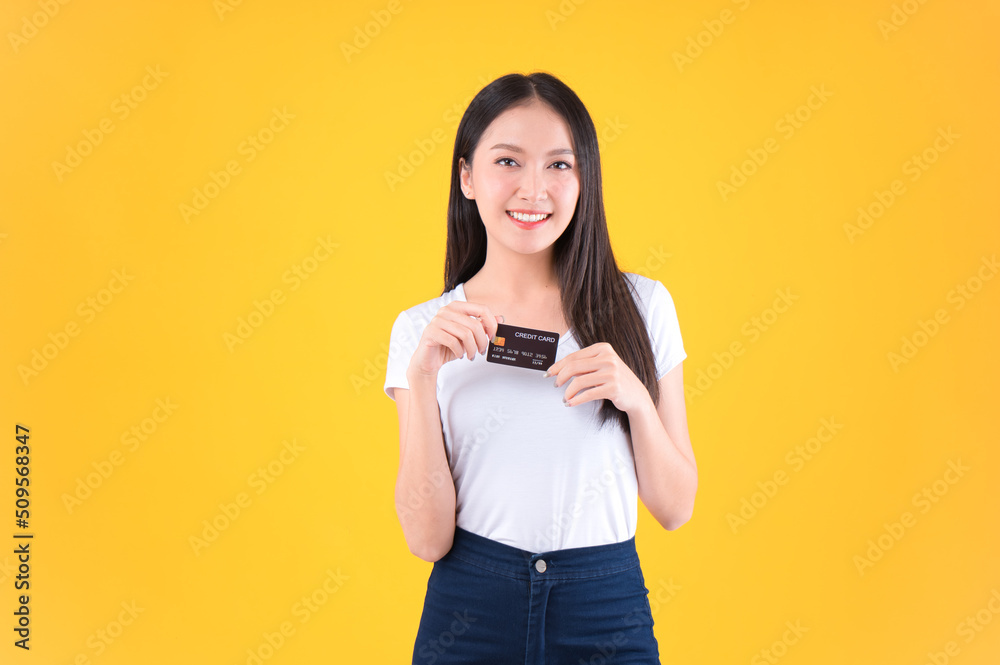 Naklejka premium Photo happy positive pretty asian woman smile showing, presenting credit card for payment or paying online business payment credit card for confident money and financial concepts yellow background.
