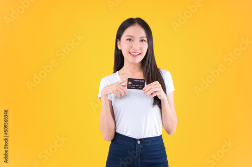 Photo happy positive pretty asian woman smile showing, presenting credit card for payment or paying online business payment credit card for confident money and financial concepts yellow background.