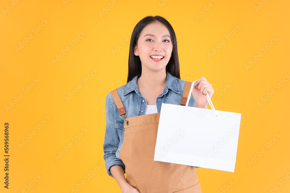 pretty asian female smile freelancer own shop show paper bags to customers buy products yellow background. pretty asian female smile freelancer own shop show paper bags to customers buy products yellow background.