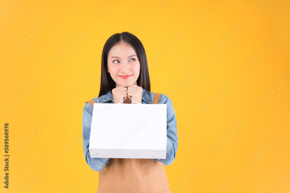 pretty asian female smile freelancer own shop show paper bags to customers buy products yellow background. pretty asian female smile freelancer own shop show paper bags to customers buy products yellow background.