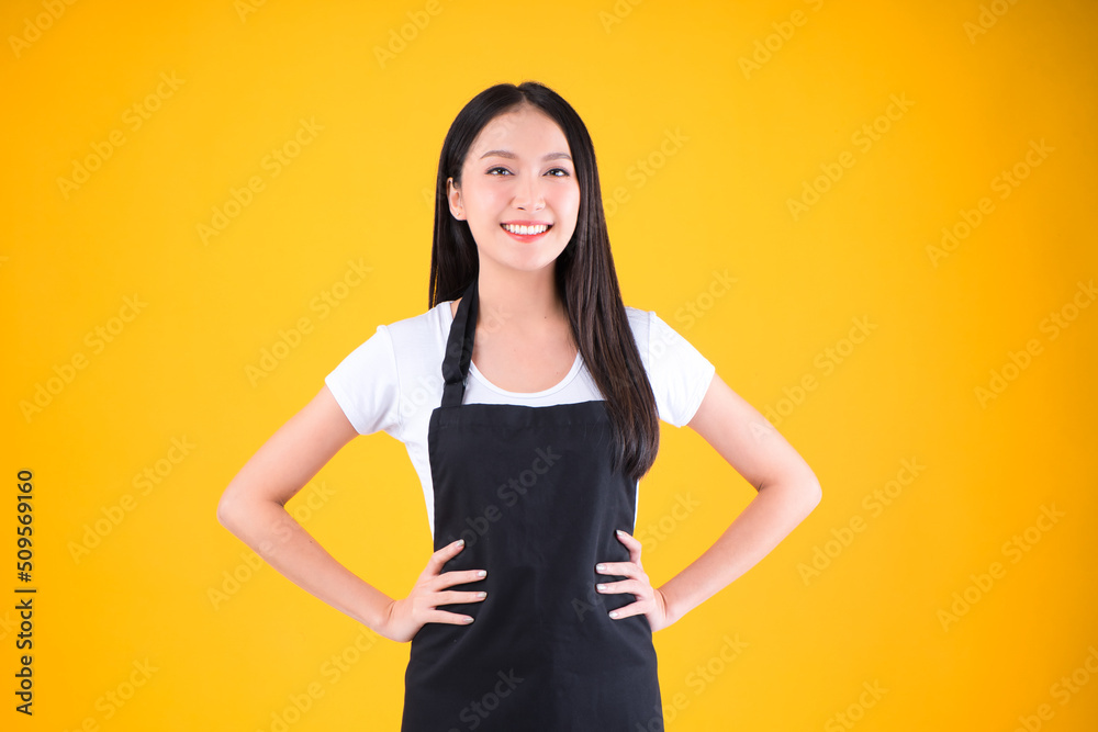 pretty asian female smile wearing black apron show and present pointing fingers copy space for your advertisement yellow background. pretty asian female smile wearing black apron show and present pointing fingers copy space for your advertisement yellow background.