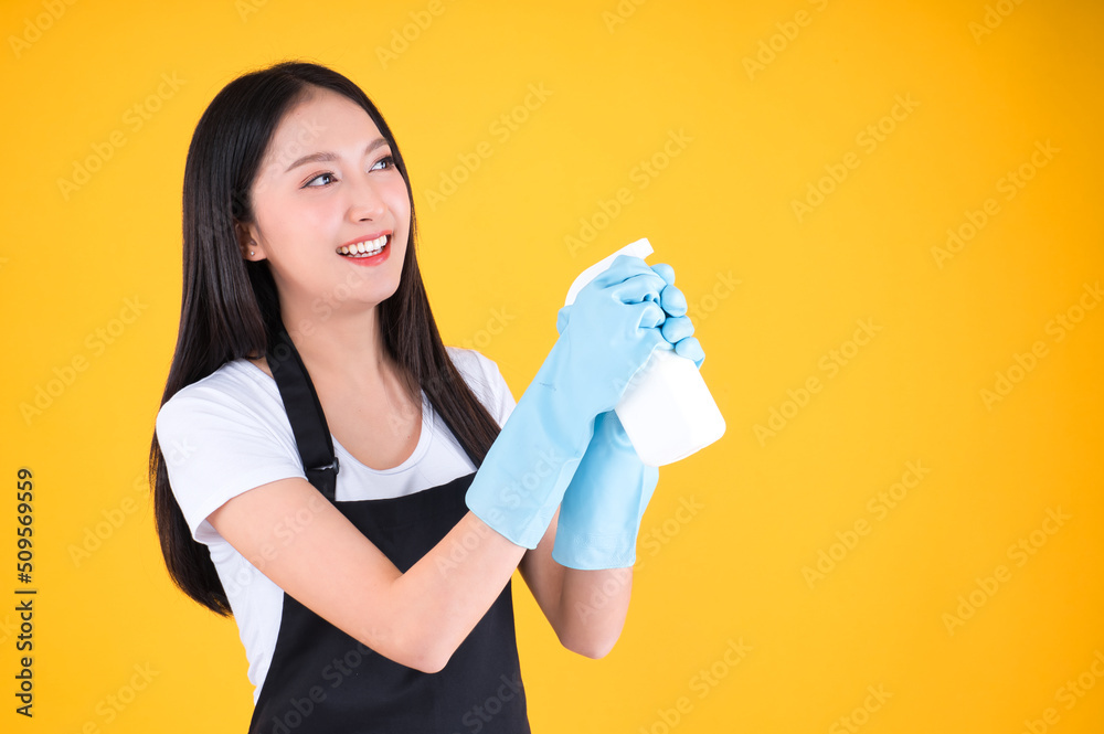 attractive asian female smile wearing black apron her hands with blue rubber gloves holding a white spray bottle poses cleaning. attractive asian female smile wearing black apron her hands with blue rubber gloves holding a white spray bottle poses cleaning.