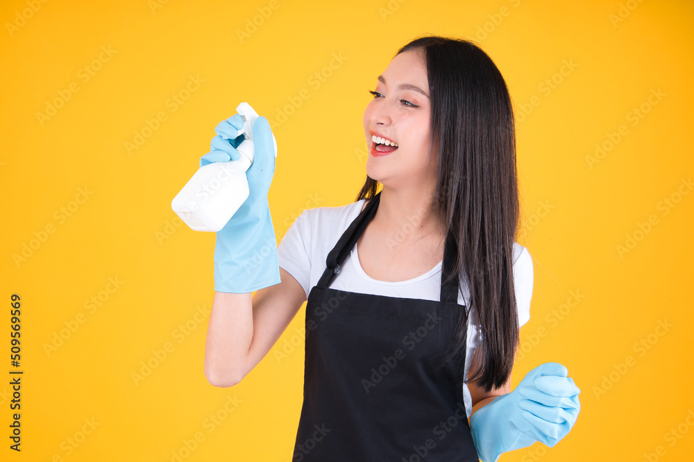 attractive asian female smile wearing black apron her hands with blue rubber gloves holding a white spray bottle poses cleaning.