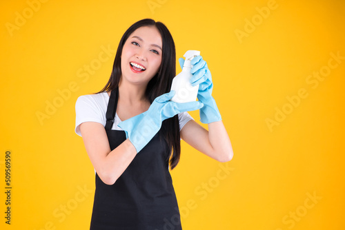 attractive asian female smile wearing black apron her hands with blue rubber gloves holding a white spray bottle poses cleaning.