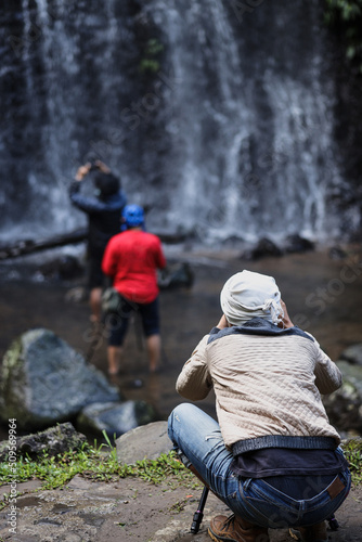 Back side of group landscape photographers capturing small waterfall. 