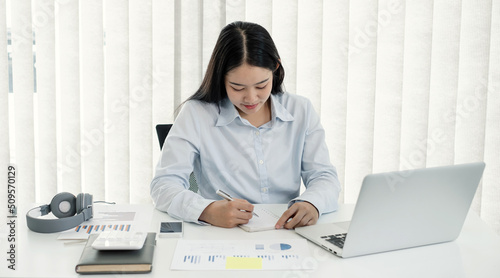 Asian woman working laptop. Successful smiling businesswoman sitting working and take note at the office © Orathai