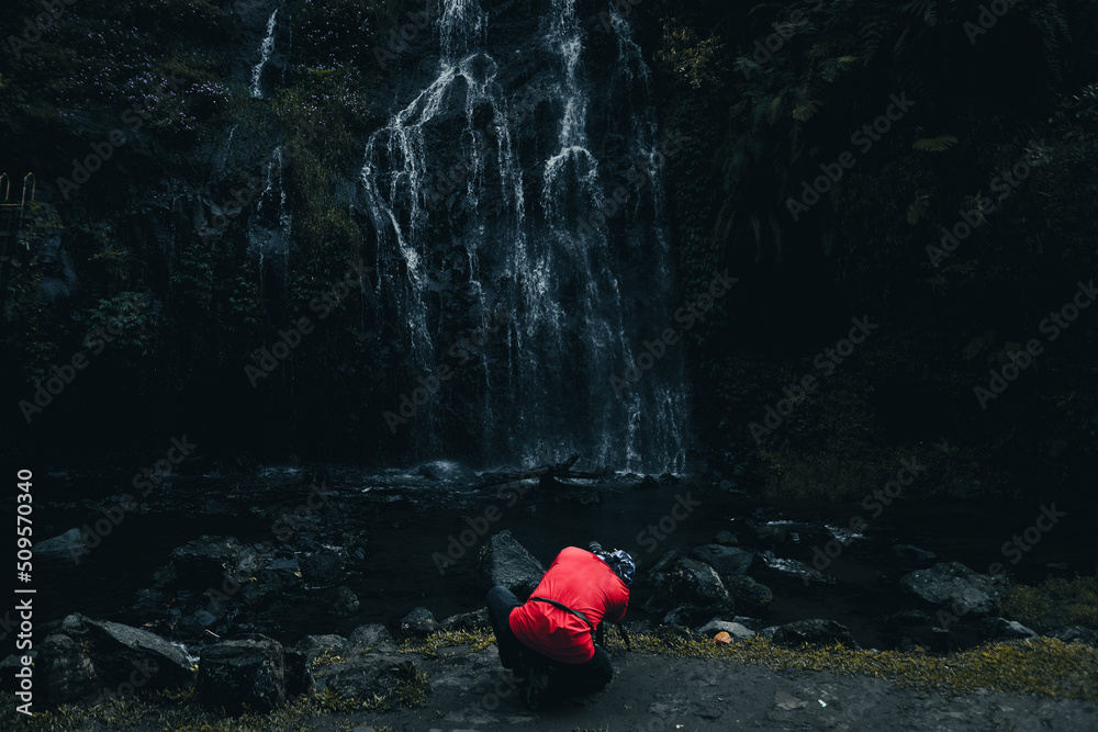 Obraz premium Back side of photographer in red t-shirt with modern camera photography capturing waterfall landscape.