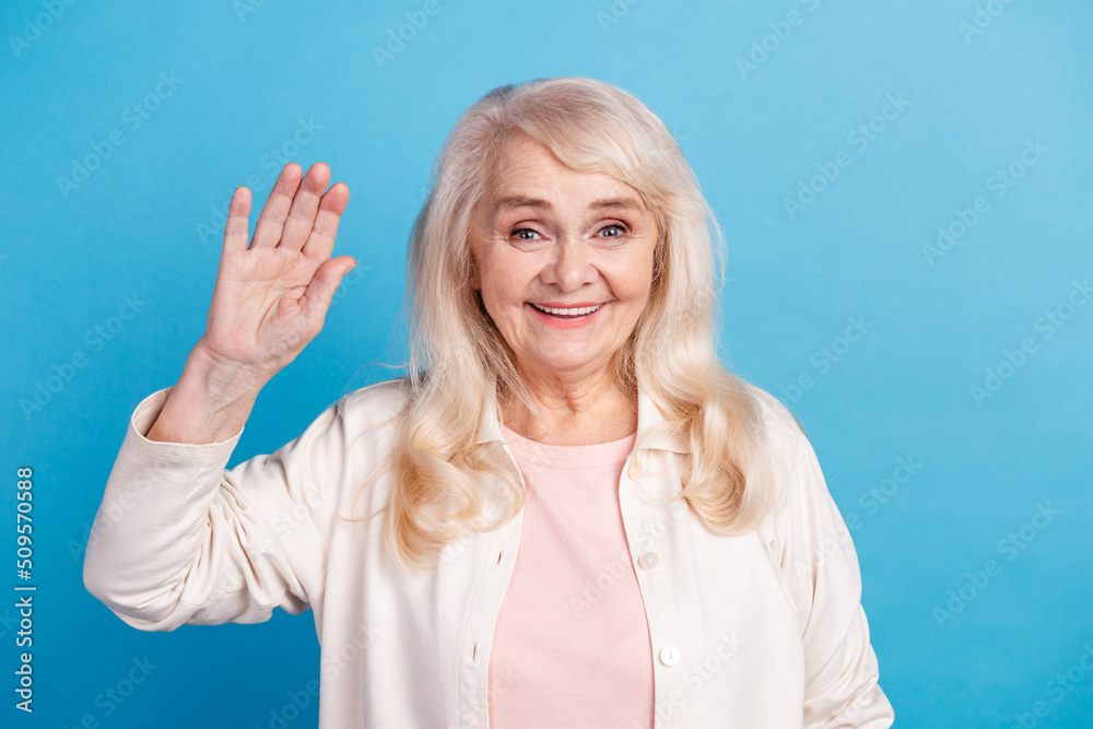 Photo of lovely charming aged woman waving hand hello meet friends isolated over blue color background Photo of lovely charming aged woman waving hand hello meet friends isolated over blue color background