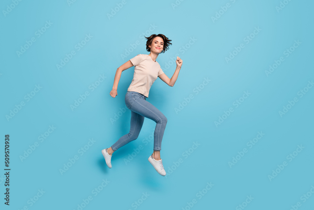 Full length photo of cute charming woman wear beige t-shirt hurrying jumping high isolated blue color background