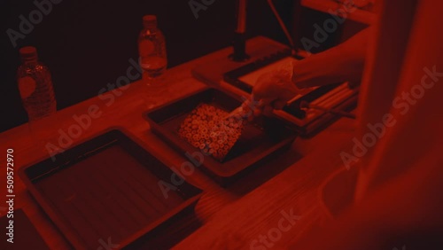 Unrecognizable male photographer using two containers with chemical solutions, placing photo inside with tongs while printing photos in darkroom