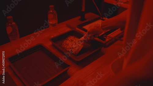 Unrecognizable male photographer using two containers with chemical solutions, placing photo inside with tongs while printing photos in darkroom photo