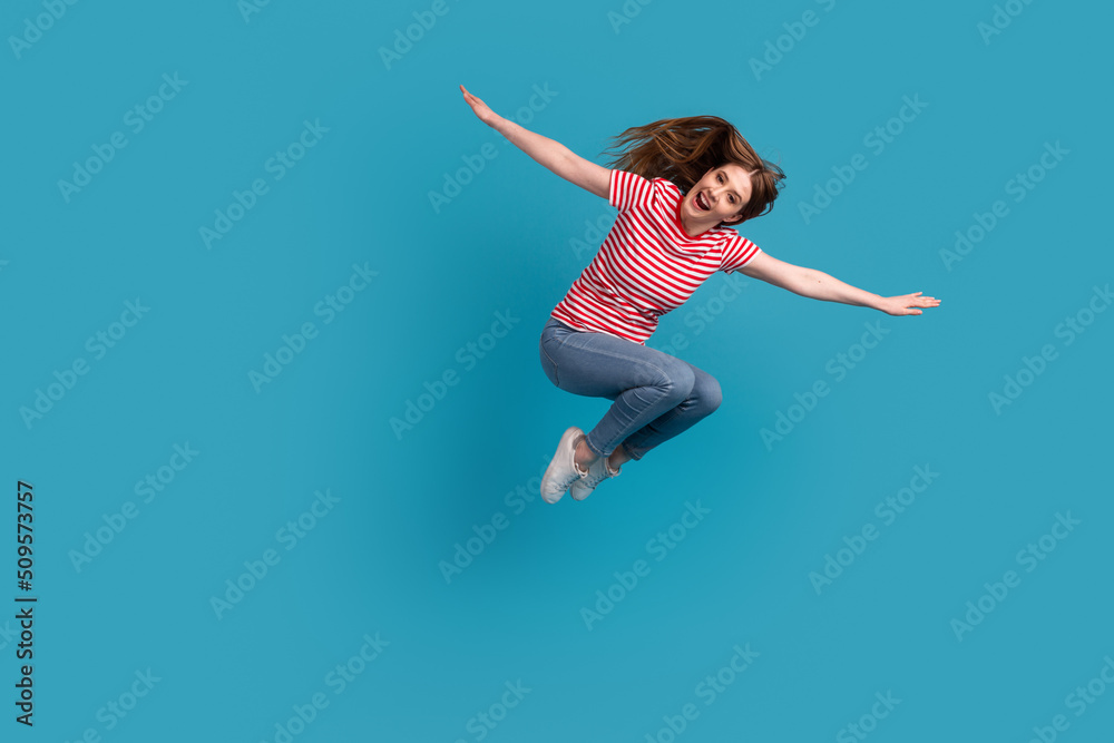 Full length profile side photo of young cheerful woman have fun jump arms wings isolated over blue color background