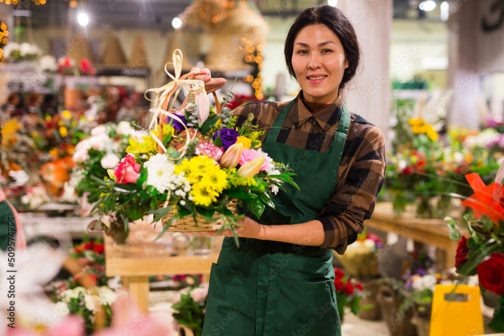 Middle age asian female florist in apron holding composition from natural flowers at flower shop