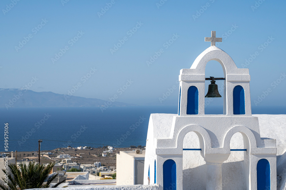 Blue and white colored Greek orthodox church, bells and cross roof, during a sunny summer day