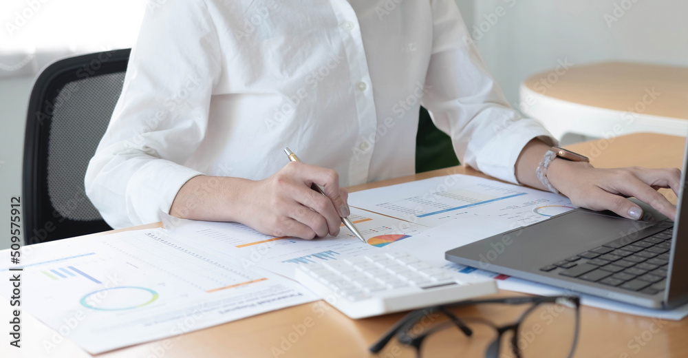 Businesswoman working at office with calculator and laptop computer calculating financial report graph data documents on desk, close up, business analysis, work process concept