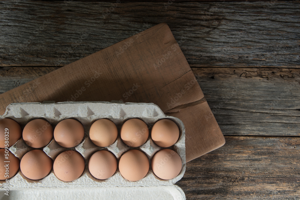 Top view of a dozen, brown eggs in a paper carton, on a cherry cutting board. Rustic barn wood background. Top view of a dozen, brown eggs in a paper carton, on a cherry cutting board. Rustic barn wood background.