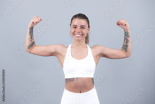 Sport woman showing strong biceps muscles. Young fit woman. Healthy lifestyle and sports concept. Isolated on gray.