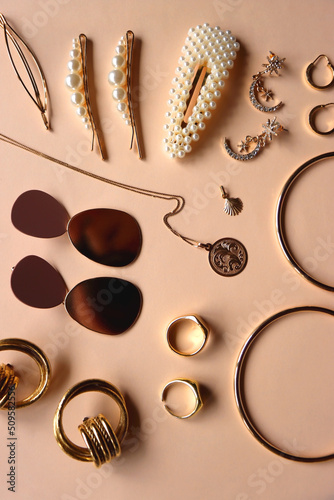 Various gold jewelry and pearl hair clips on peach colored background. Flat lay.