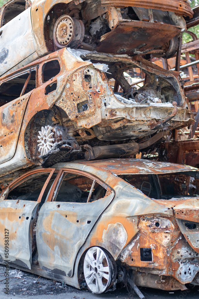 Fototapeta premium A view of burnt-out cars after rocket attacks by the Russian military. War of Russia against Ukraine. Civil vehicle after the fire. Cemetery of cars in the city of Irpin. Rusty pile of metal.