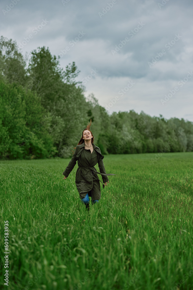 a beautiful woman in a long raincoat runs across a field in high grass in spring in cloudy weather a beautiful woman in a long raincoat runs across a field in high grass in spring in cloudy weather