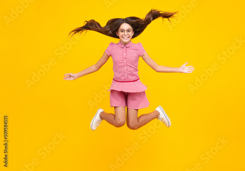 Full length cheerful teenager kid jump enjoy rejoice win isolated on yellow background. Small child girl in summer dress jumping. Amazed teen girl. Excited expression, cheerful and glad.