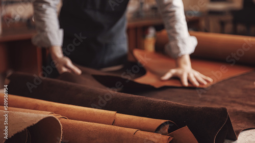 Man shoemaker hold different rolls natural leather brown, working with textile in workshop photo
