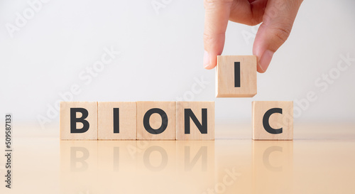 Technology applied between doctors and engineers concept. Technology advance, innovation. Hand puts wooden cubes with BIONIC on table.