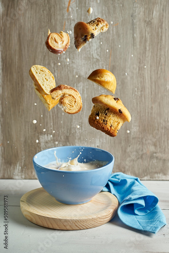 blue bowl with with splashes of milk flying chocolate muffins, palm tree,and milk bun on a rustic grey background. food art