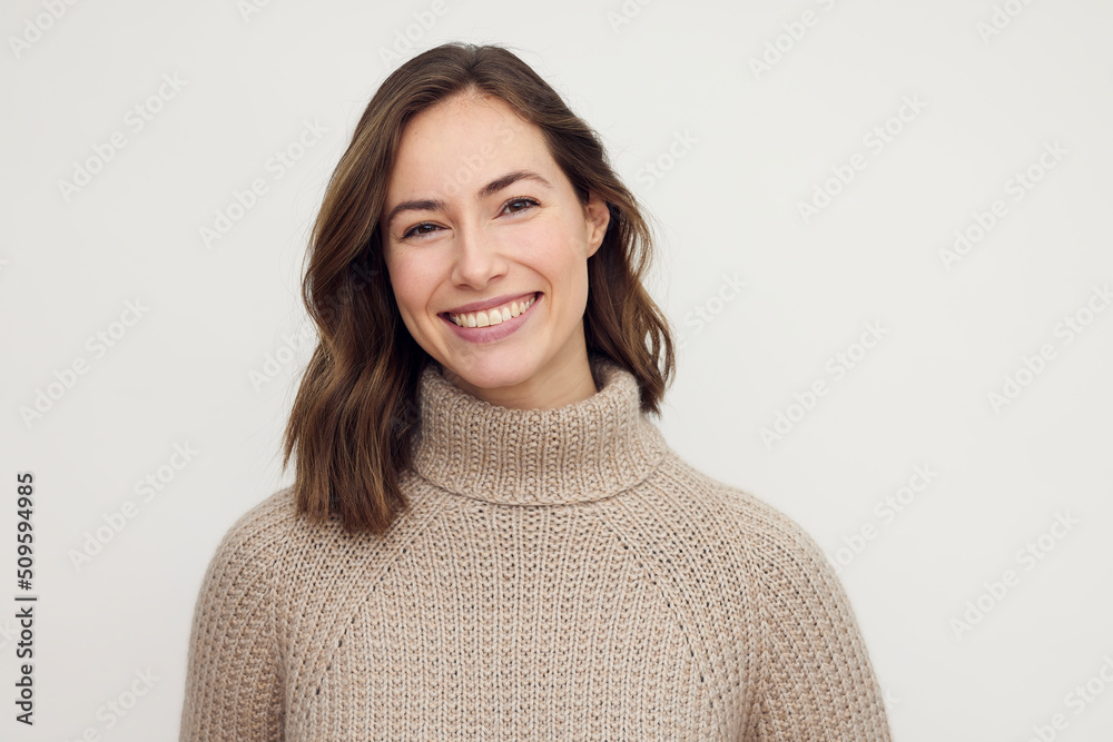 Portrait of a smiling brunette woman in a warm beige sweater, looking happy in camera.